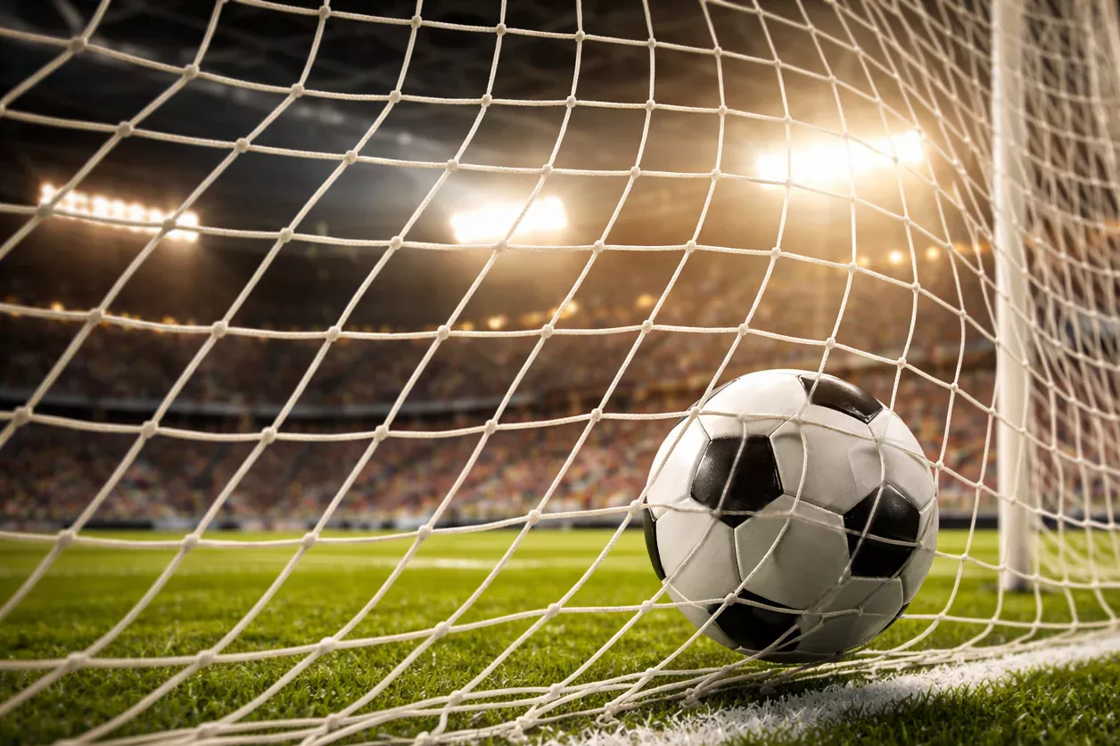 Red de portería de fútbol vista desde dentro con el balón entrando y el estadio iluminado al fondo